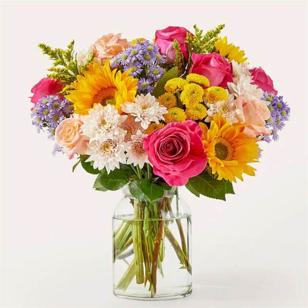 Mixed bouquet of roses, sunflowers, and daisies in a clear glass vase