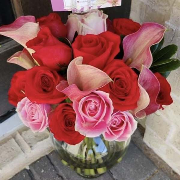 Bouquet of red and pink roses with pink calla lilies in a glass vase