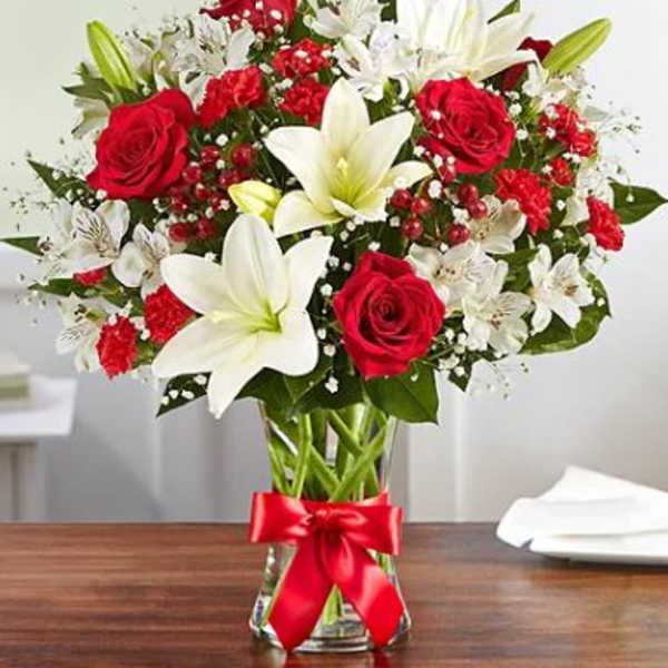 Bouquet of red roses and white lilies in a glass vase with a red ribbon