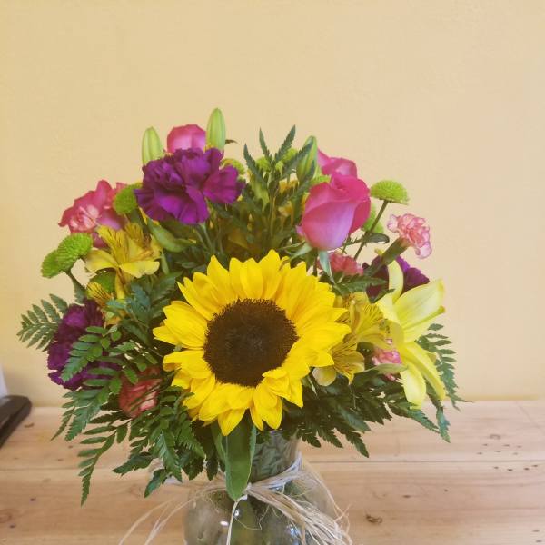 Mixed bouquet with a sunflower, pink roses, and purple flowers in a glass vase