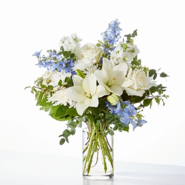 White lilies and roses with blue flowers in a clear glass vase