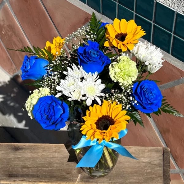 Bouquet of blue roses, sunflowers, and white daisies in a glass vase