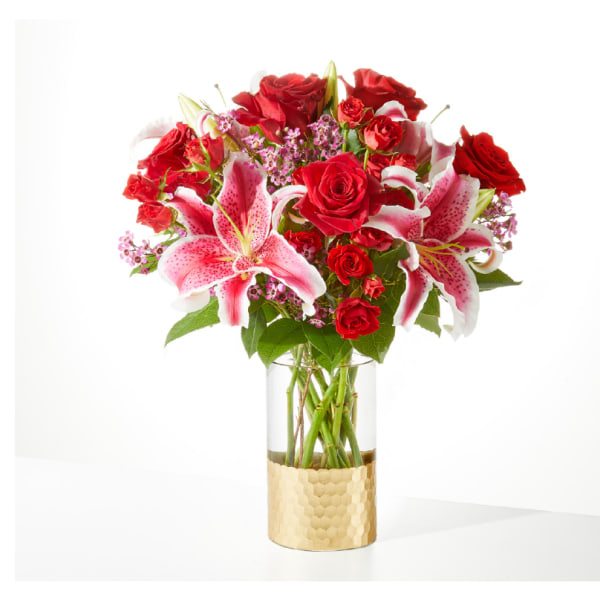 Red roses and pink lilies arranged in a glass vase with a gold base