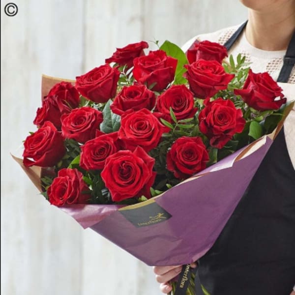Large bouquet of red roses wrapped in purple paper, held by a person in a black apron