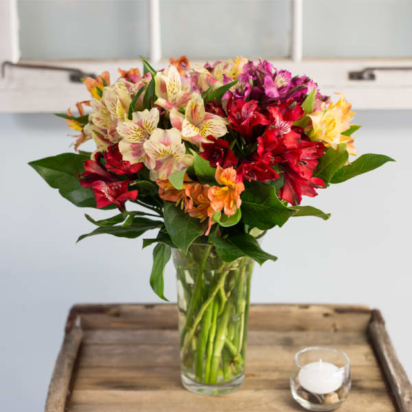 Mixed bouquet of alstroemeria in a glass vase beside a small candle