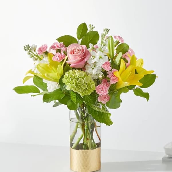 Pink roses and yellow lilies in a glass vase with a gold base