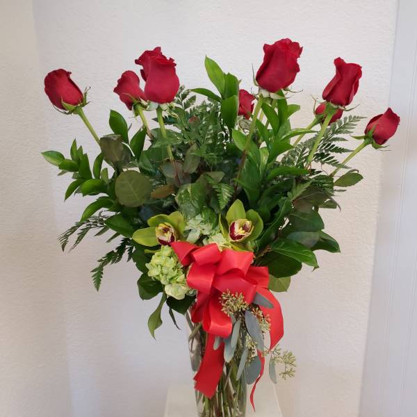 Red roses and green orchids in a glass vase with a red ribbon