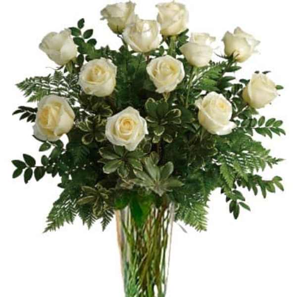 White roses arranged in a tall clear glass vase with greenery