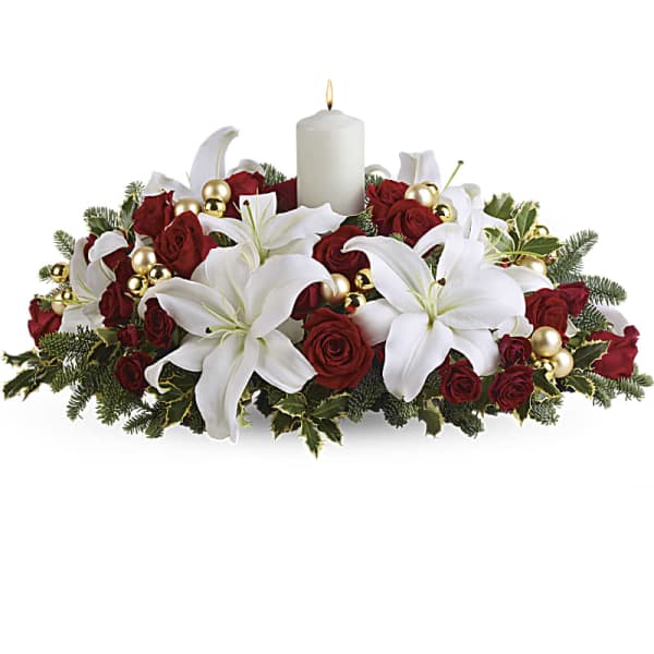 White lilies and red roses arranged around a lit pillar candle