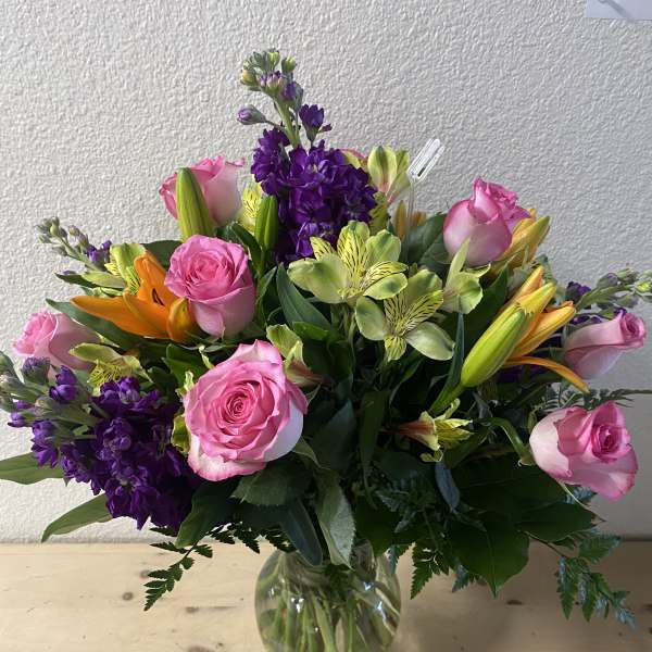 Mixed bouquet of pink roses, purple flowers, and lilies in a glass vase