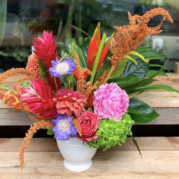 Colorful tropical bouquet in a white vase with pink, orange, purple, and green blooms