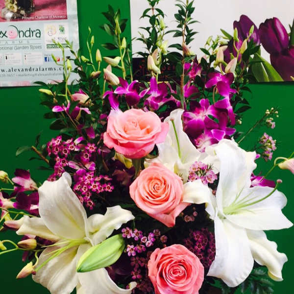 Pink roses and white lilies in a white vase with purple orchids