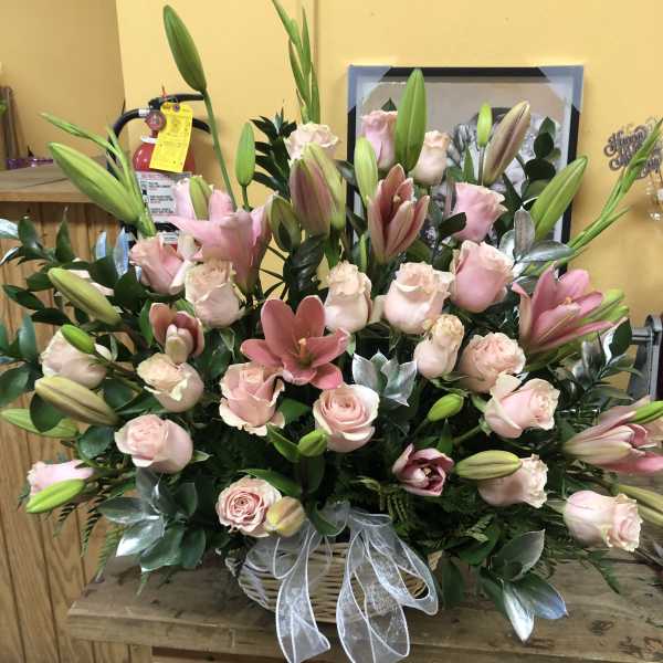 Pink roses and lilies arranged in a basket with a white ribbon