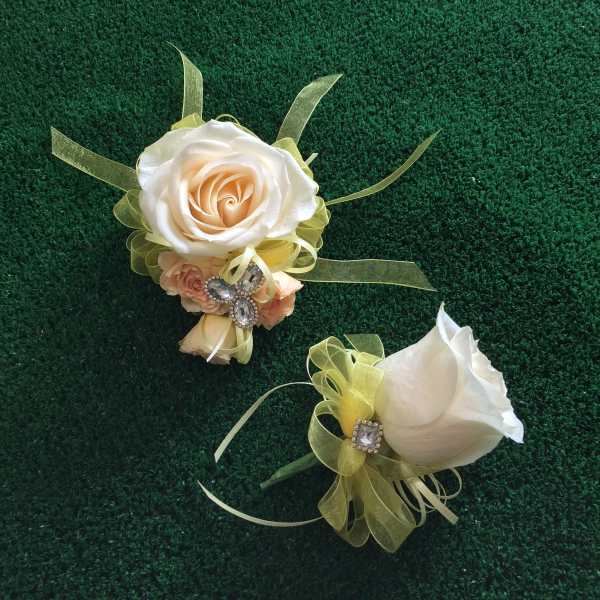 Two white rose corsages with pale green ribbon accents on a dark green surface
