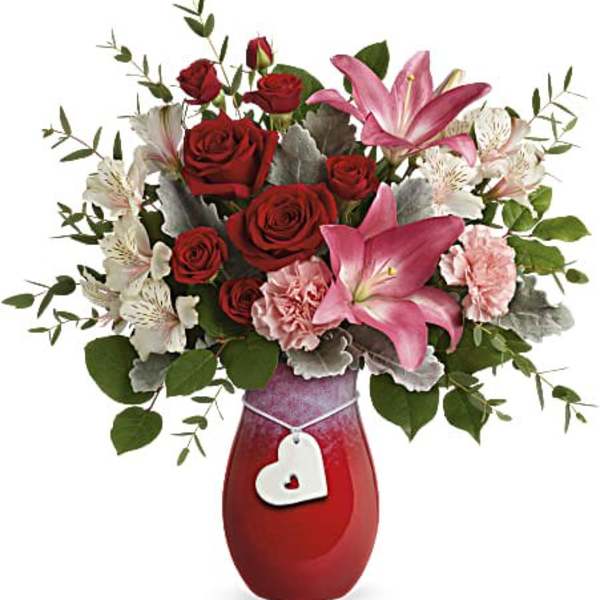 Red roses and pink lilies in a red vase with a heart tag