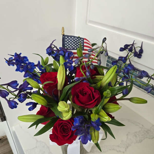 Red roses and blue flowers in a clear vase with an American flag