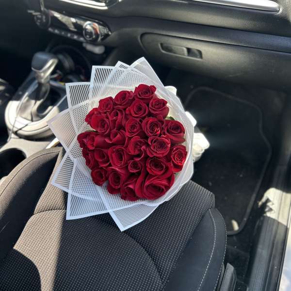 Bouquet of red roses wrapped in white paper on a car seat