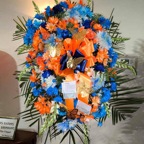 Large standing floral spray in blue, orange, and white with ribbons and butterflies