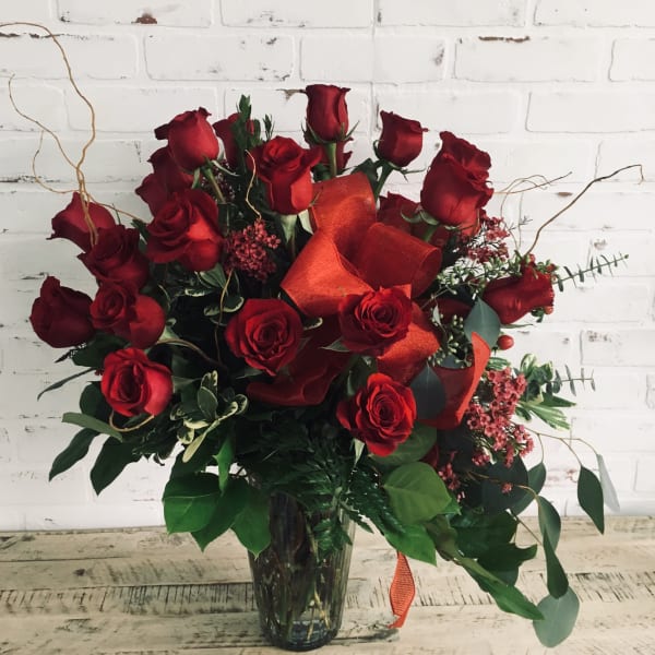 Red roses arranged in a clear glass vase with orange ribbon accents