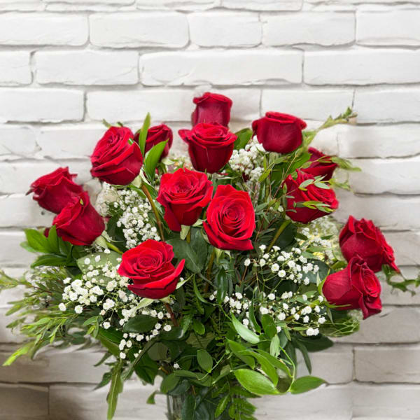 Red roses arranged in a clear glass vase with white filler flowers