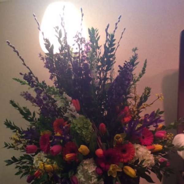 Tall mixed flower arrangement with bright tulips and gerbera daisies in a dark vase