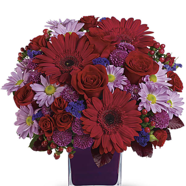 Bouquet of red roses and purple daisies in a clear square vase