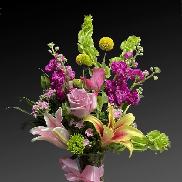 Pink and yellow mixed flower arrangement in a glass vase with a pink ribbon