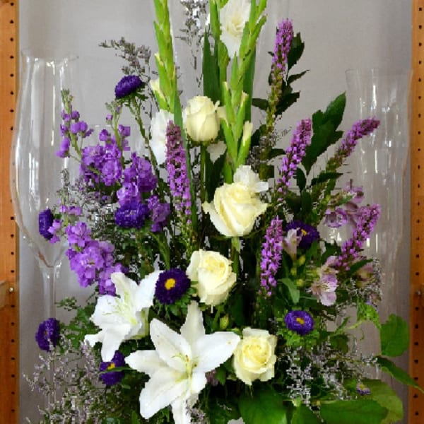 Tall white vase arrangement with white lilies, cream roses, and purple flowers