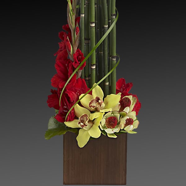 Red flowers and yellow orchids arranged with bamboo in a wooden container