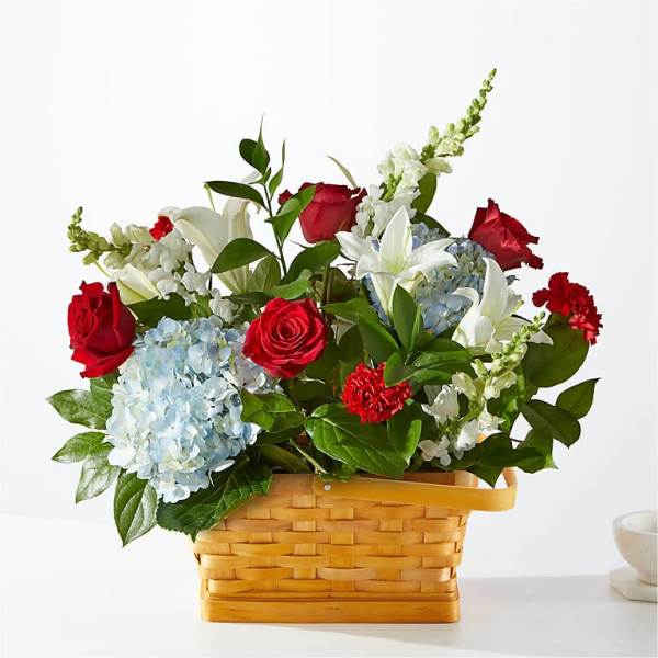 Basket arrangement of red roses, white lilies, and blue hydrangeas