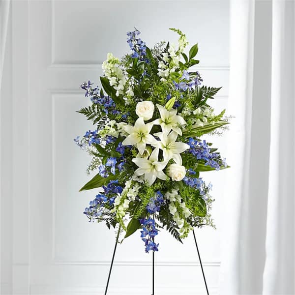 Standing floral spray with white lilies and blue flowers on a black easel
