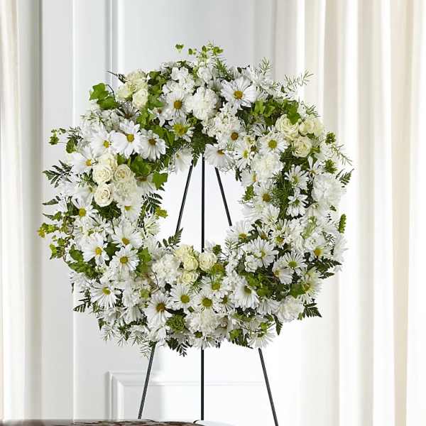 White floral wreath on a black stand with daisies and roses