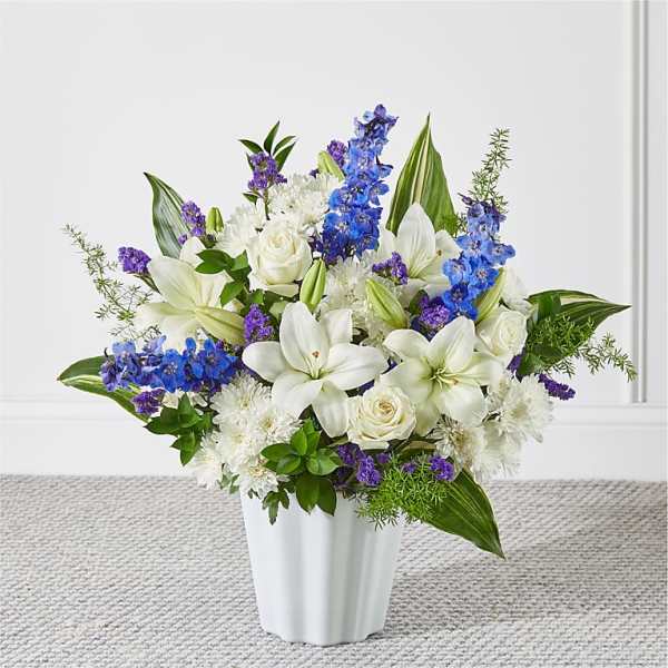 White lilies, roses, and blue delphinium in a white vase