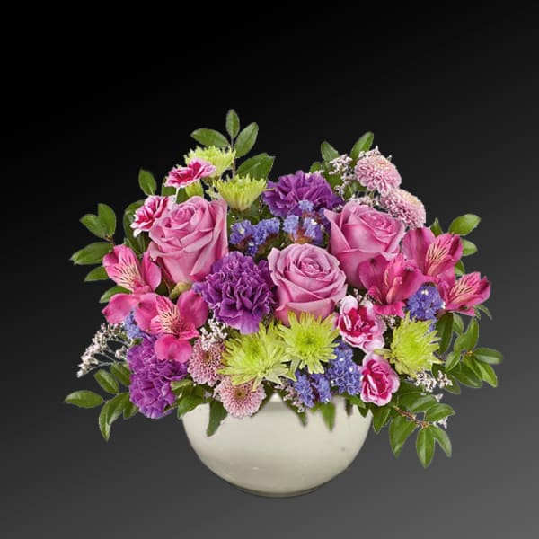 Pink and purple mixed flower arrangement in a white bowl vase