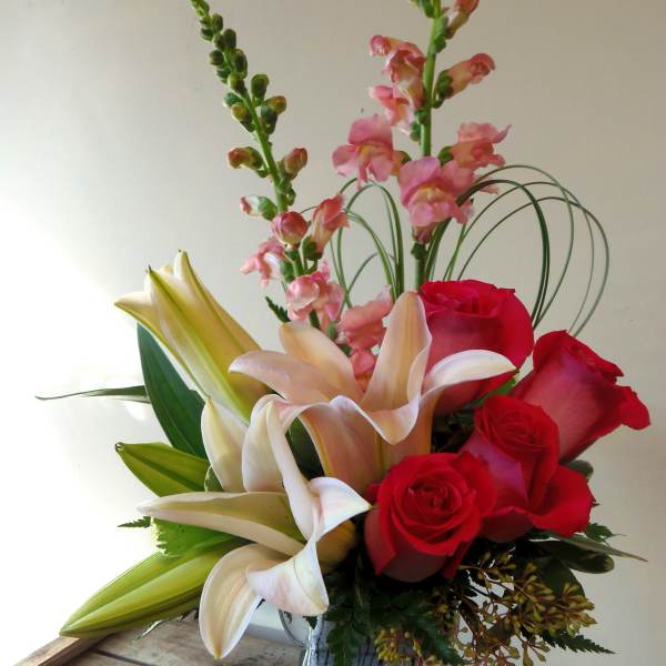 Bouquet of red roses, lilies, and pink snapdragons in a glass vase