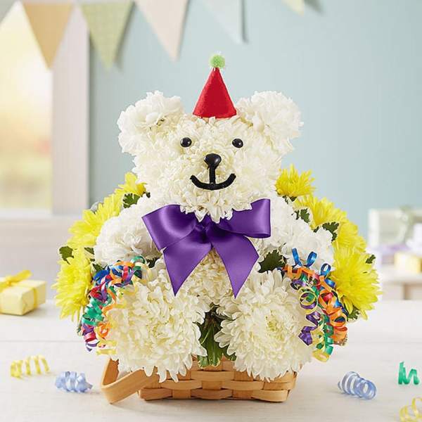 White flower teddy bear in a basket with a purple bow and party hat