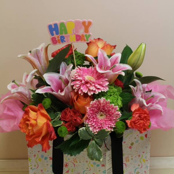 Birthday flower arrangement in a gift bag with pink lilies and roses
