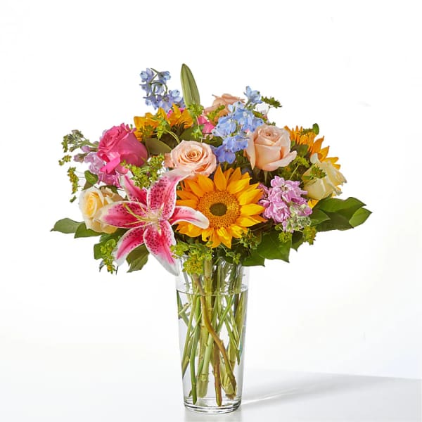 Mixed bouquet of roses, lilies, and sunflowers in a clear glass vase