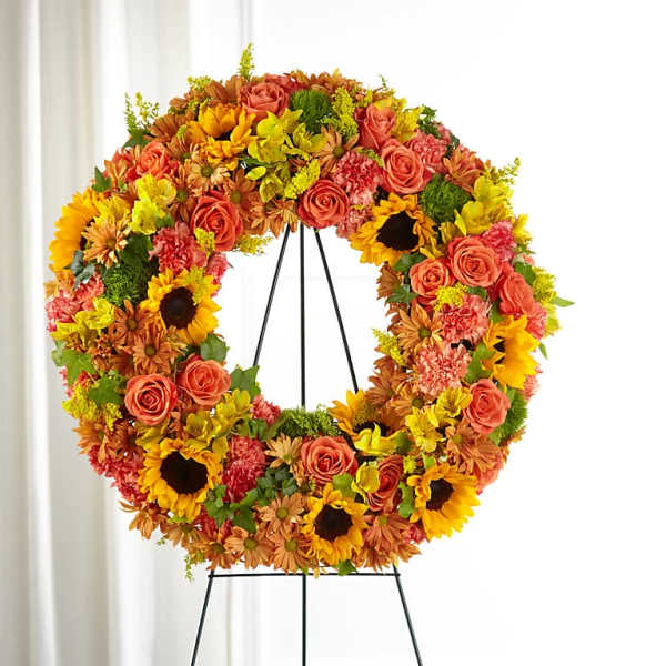 Circular floral wreath with roses, sunflowers, and mums on a black stand