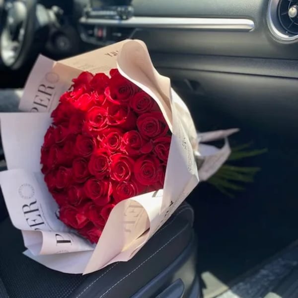 Bouquet of red roses wrapped in white paper on a car seat