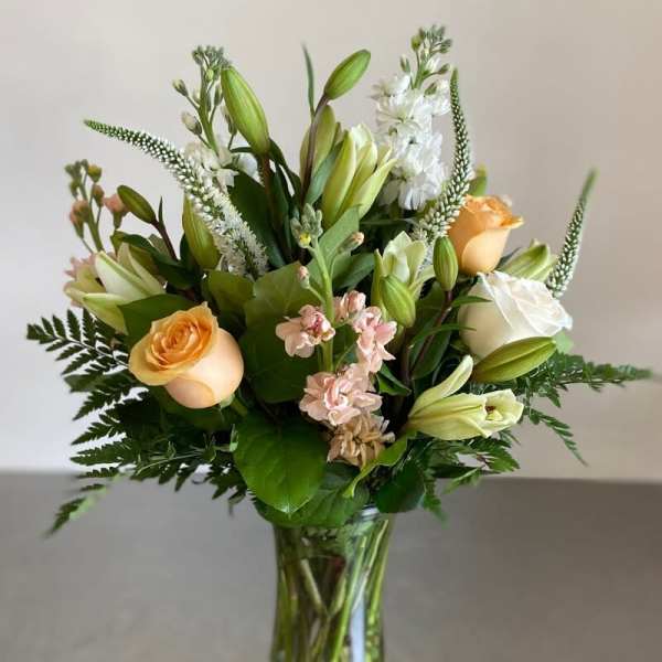 Tall bouquet of peach roses, white lilies, and soft pink flowers in a clear glass vase