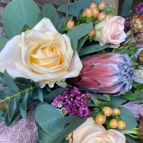 Bouquet with cream roses, a pink protea, and purple filler flowers
