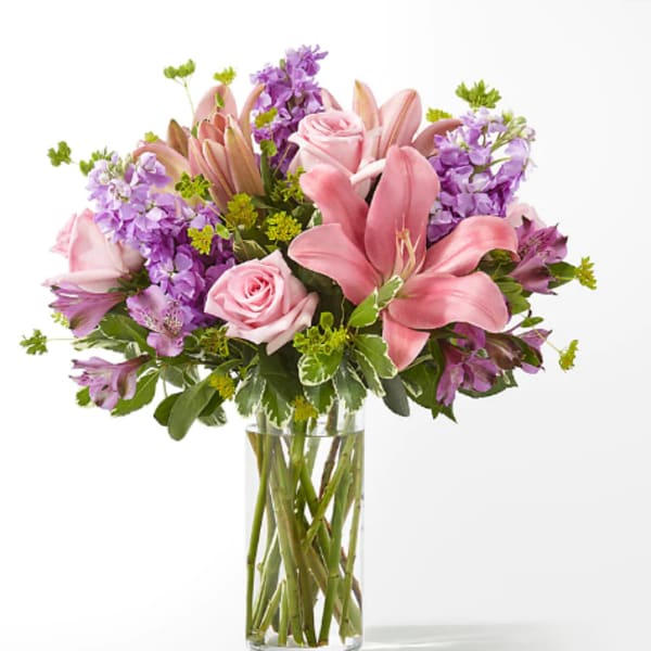 Pink lilies and roses in a clear glass vase with purple flowers