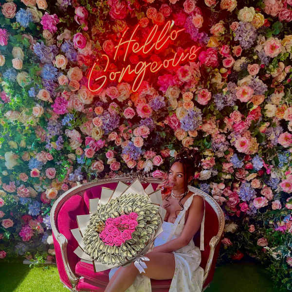 Woman seated on a pink sofa holding a bouquet against a flower wall