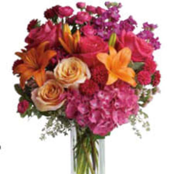 Mixed bouquet of pink, orange, and purple flowers in a clear glass vase