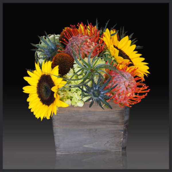 Bright mixed bouquet with sunflowers and pincushion protea in a wooden container