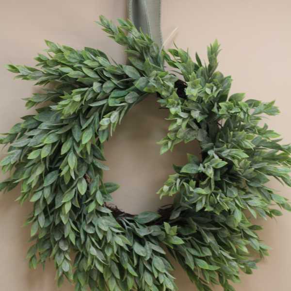 Green leafy wreath with a ribbon bow hanging on a wall