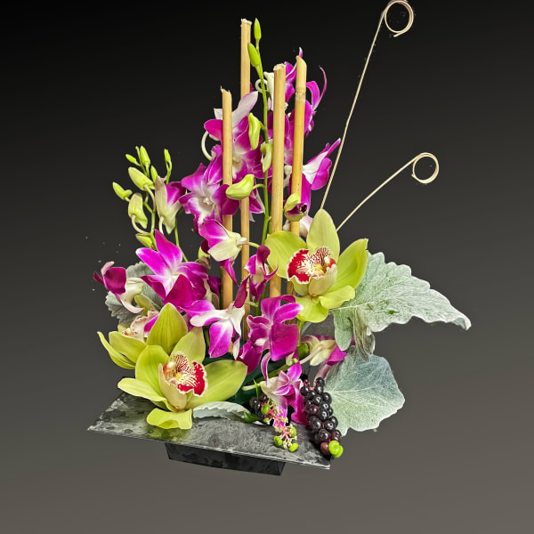 Tall orchid arrangement in a dark rectangular vase with decorative bamboo loops