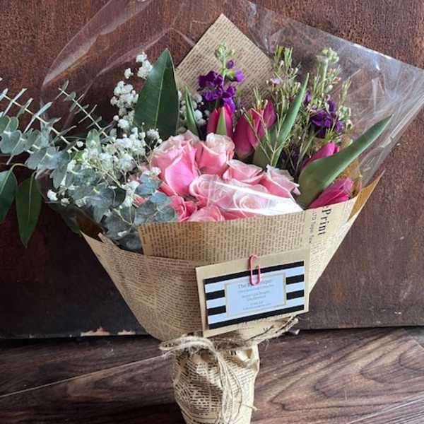 Bouquet of pink roses and purple flowers wrapped in newspaper-style paper