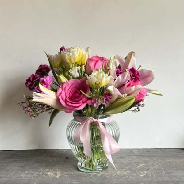 Pink and white mixed bouquet in a clear glass vase with a pink ribbon